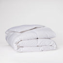 A neatly made bed features the Sienna Living Summer 80% Duck Down 20% Duck Feather Quilt and white pillows, set atop a light-colored rug against a plain blue wall.