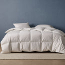 A neatly made bed features the Sienna Living Summer 80% Duck Down 20% Duck Feather Quilt and white pillows, set atop a light-colored rug against a plain blue wall.