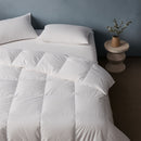 A neatly made bed features the Sienna Living Summer 80% Duck Down 20% Duck Feather Quilt and white pillows, set atop a light-colored rug against a plain blue wall.
