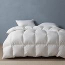 A neatly made bed features the Sienna Living Winter 80% Goose Down 20% Goose Feather Quilt from Sienna Living, paired with two pillows, set against a plain light blue wall on a light-colored carpeted floor.