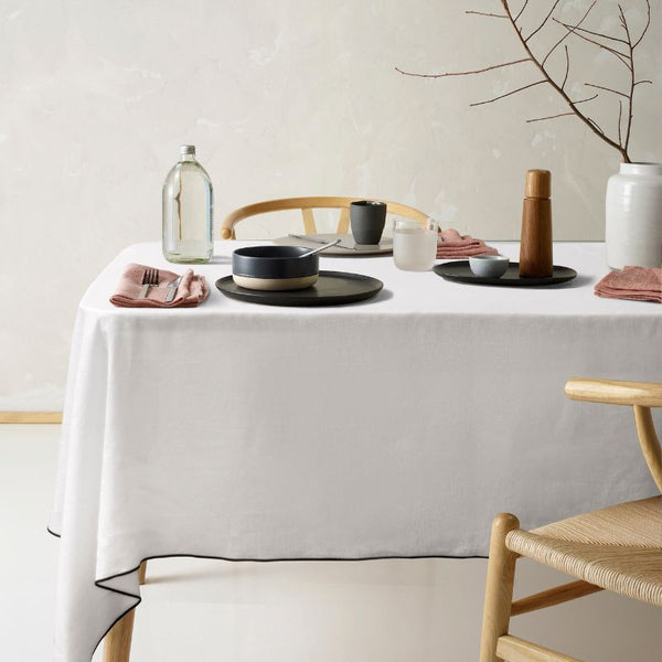 Vintage Design Atelier Linen Cotton White Tablecloth with black edge trim styled on dining table.
