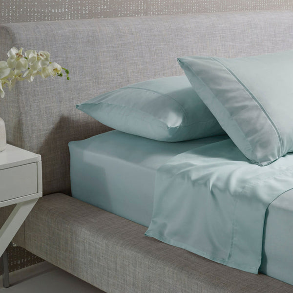 alt="A blue and plain cotton sheet set in a luxurious bedroom"