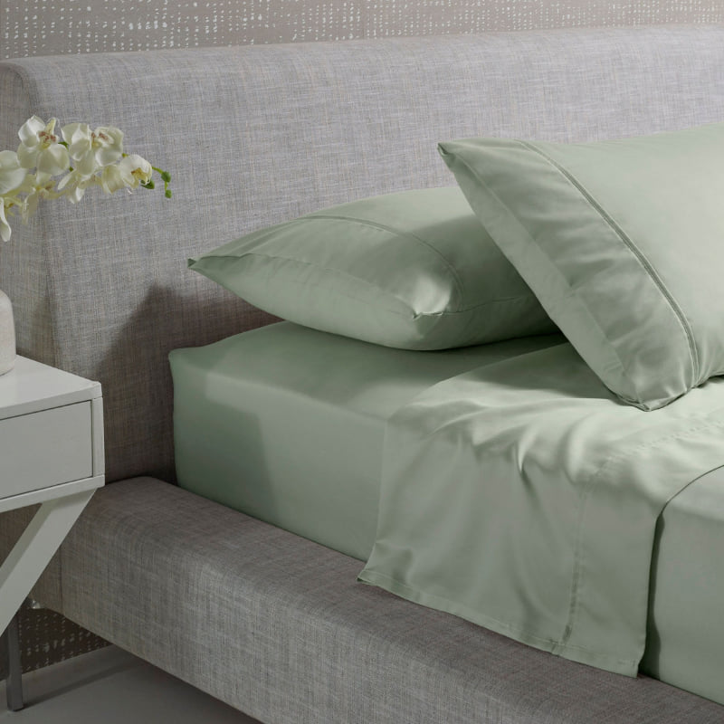 alt="A green and plain cotton sheet set in a luxurious bedroom"