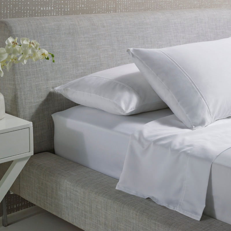 alt="A white and plain cotton sheet set in a luxurious bedroom"