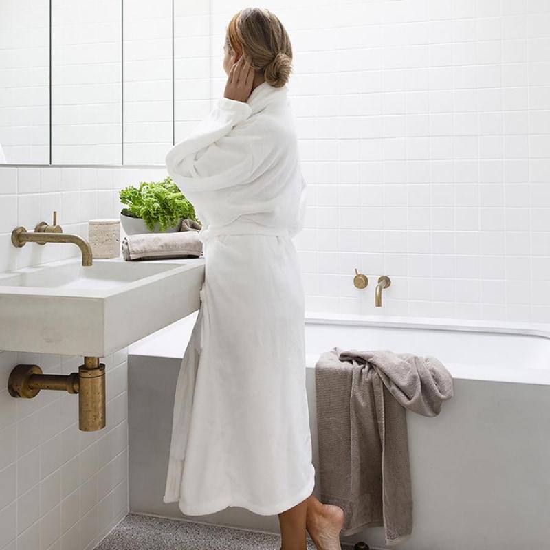 alt="A woman wearing a white microplush robe, looking at herself in the mirror"