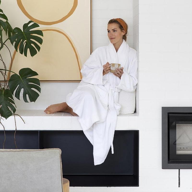 A woman wearing a microplush white robe drinking coffee while sitting