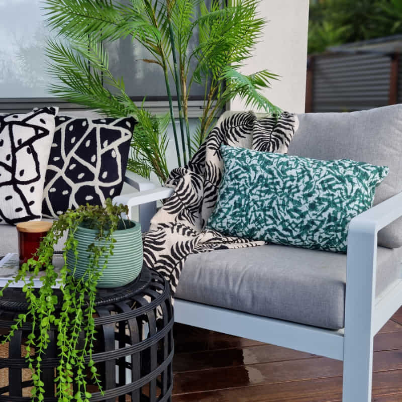 alt="A coastal vibe cushion with captivating double-sided foliage design, crafted from premium soft cotton and featuring impeccable chain-stitched detailing in an outdoor space"