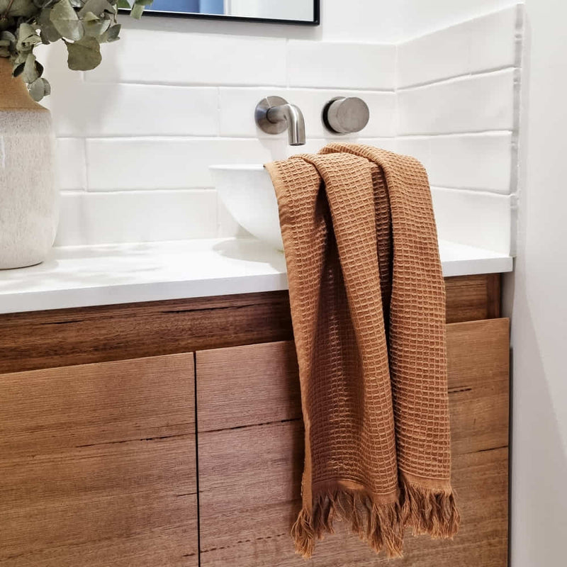 alt=" A 100% cotton, waffle weave front, terry fabric underside, and decorative fringe accents hand towels  in a sink area"