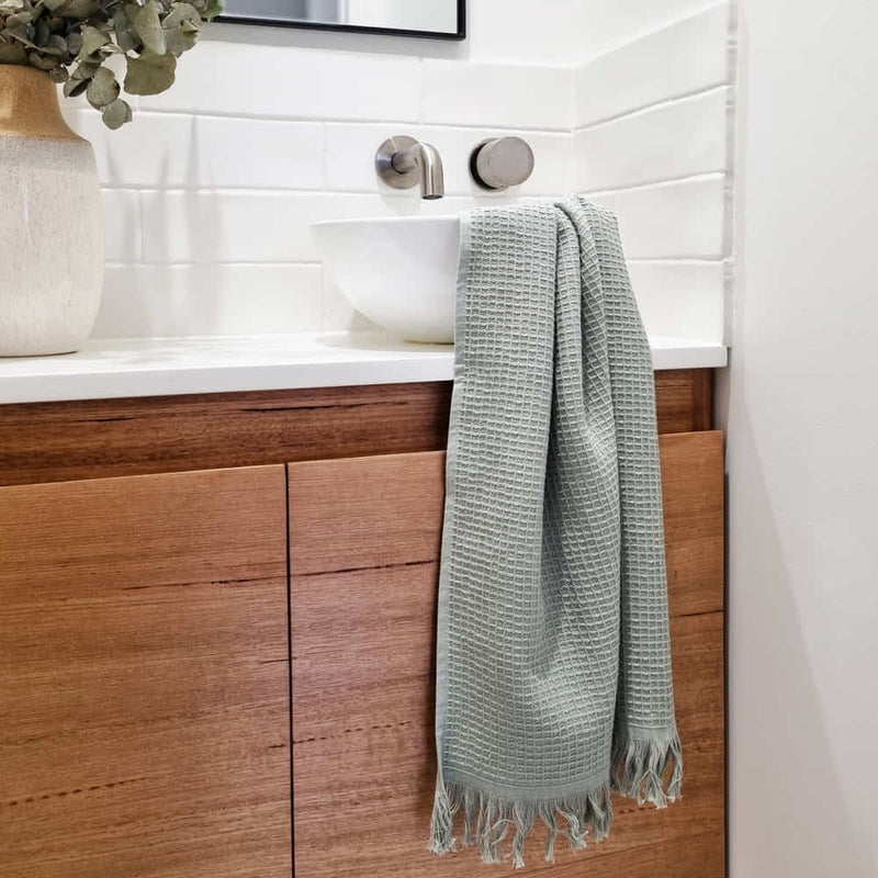 alt=" A 100% cotton, waffle weave front, terry fabric underside, and decorative fringe accents hand towels in a sink area"