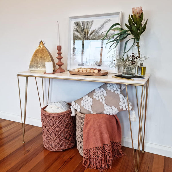 alt text="J. Elliot Luisa Clay Basket, adorned with a cosy throw and pillow beneath a console table."