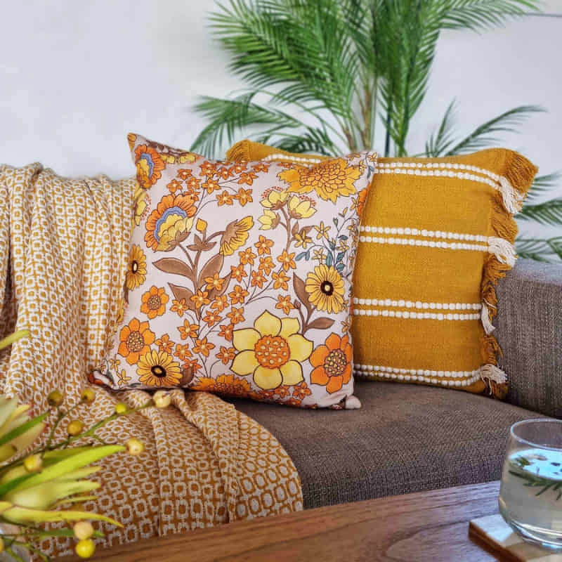 alt="A yellow multicoloured cushion featuring beautiful and bold florals in a cosy sofa"