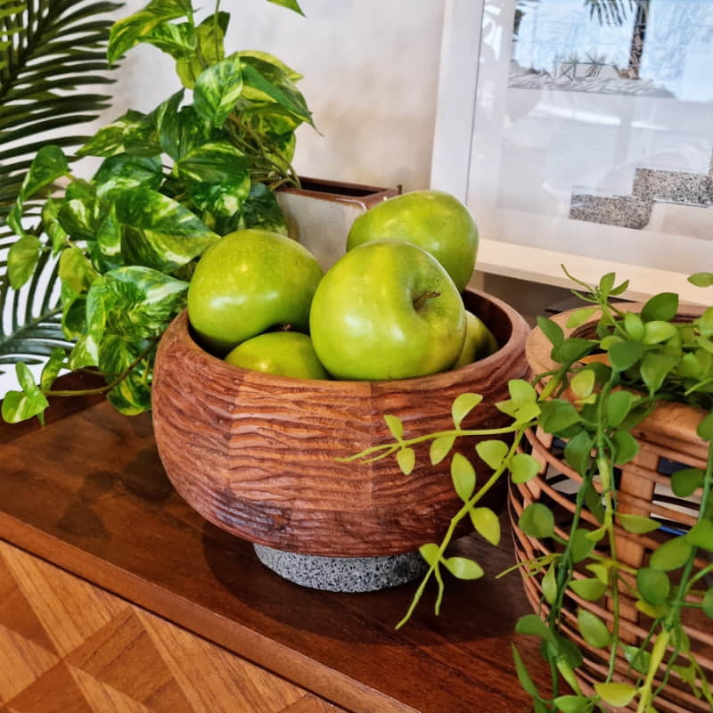 alt="A fruit bowl crafted from carved acacia wood for a touch of texture, the bowl rests upon a slap of terrazzo pairing beautifully with the brown tones of the acacia in a dining area." 