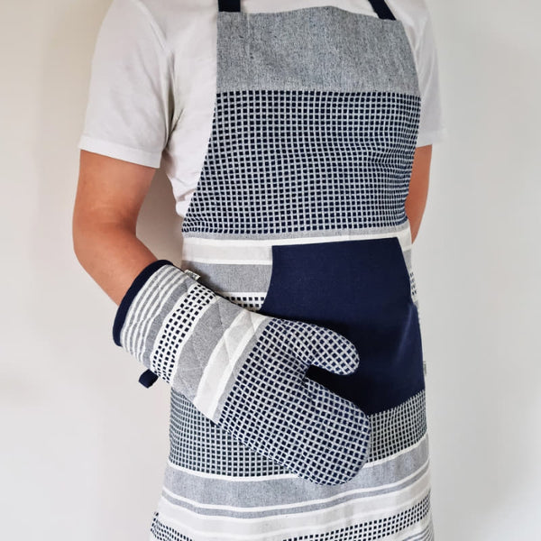 alt="A navy and grey apron features a combination of stripes and stitches in a neutral colour palette pair with glove."