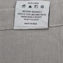 Back tag details on Venice grey linen napkin, showcasing practicality for effortless garment care.