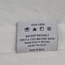 Back tag details on Venice white linen napkin, showcasing practicality for effortless garment care.