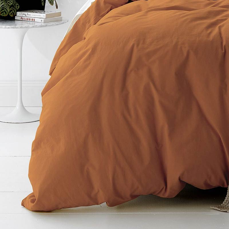 alt="A cosy bed with an orange quilt cover and a white nightstand. Elevate your bedroom with this stylish and comfortable quilt cover set.