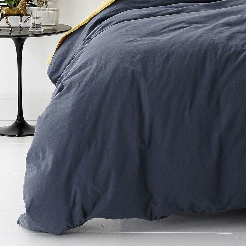 alt="A cosy bed with a blue quilt cover and a white nightstand. Elevate your bedroom with this stylish and comfortable quilt cover set.